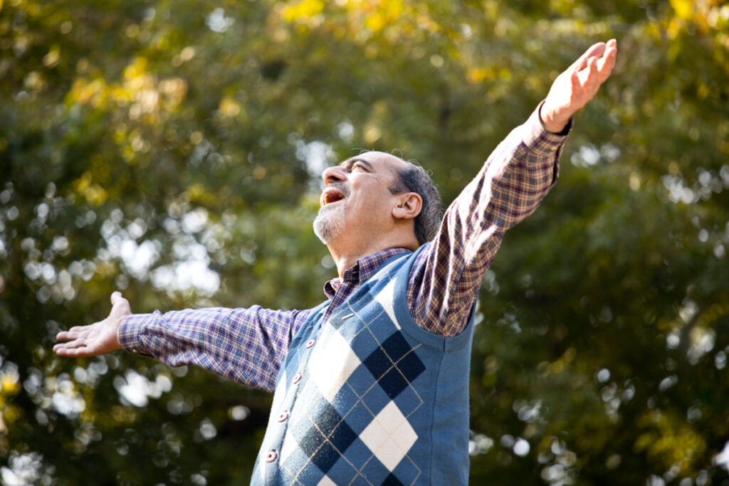 Homem idoso de braços abertos respirando ar puro